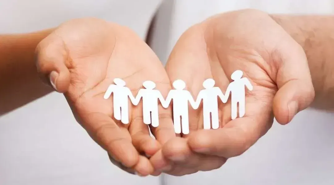 A person is holding a group of paper people in their hands.