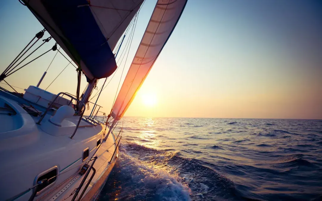 A sailboat is sailing in the ocean at sunset.