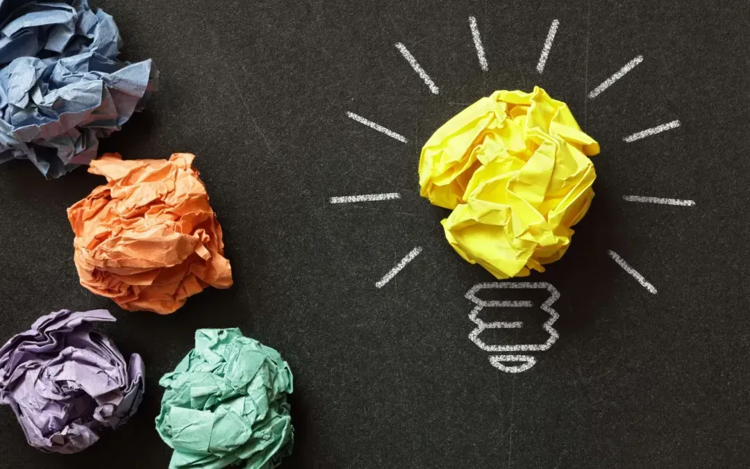 A light bulb made out of crumpled paper on a blackboard.