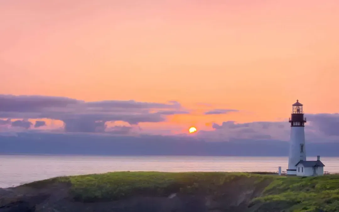 A lighthouse on a cliff overlooking the ocean at sunset.