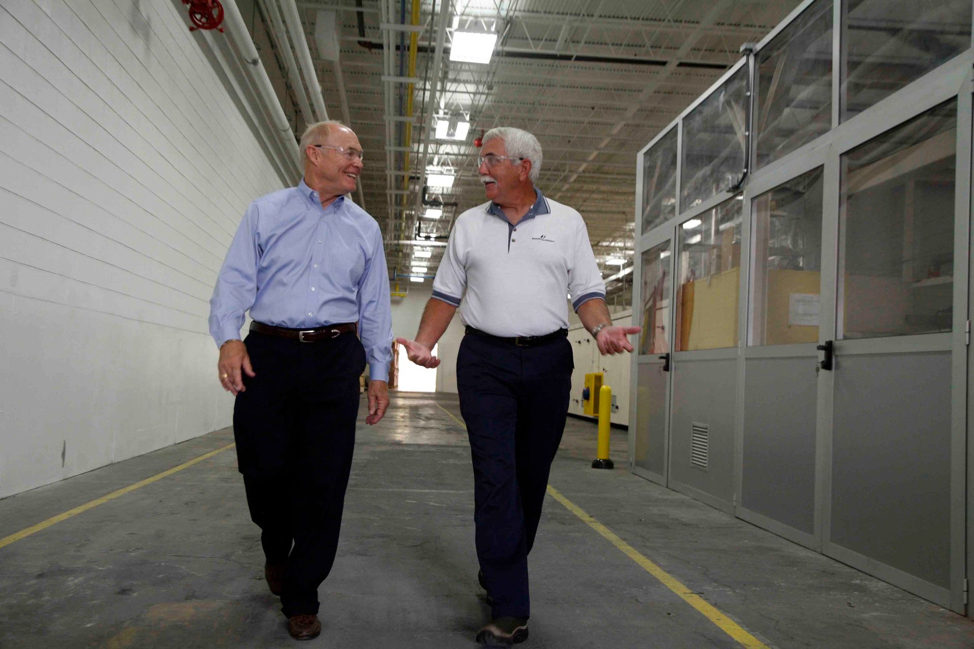 Two men are walking down a hallway and talking to each other