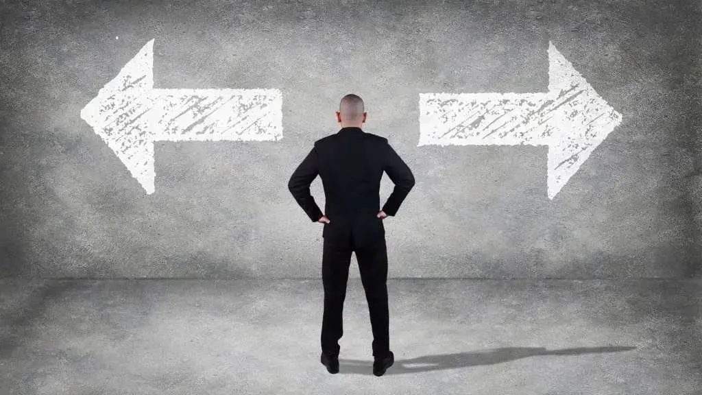 A man in a suit is standing in front of two arrows on a wall.