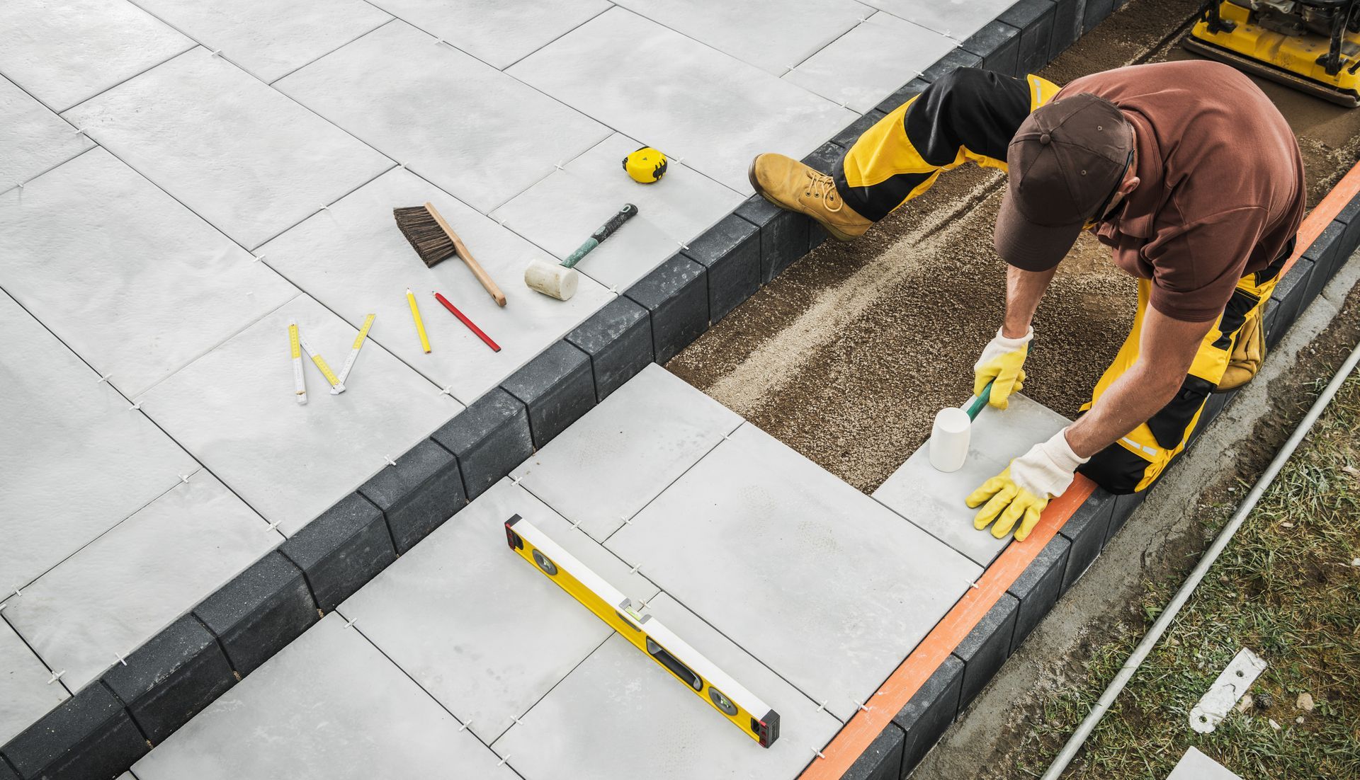 Man laying grey paving stones with tools on the side.