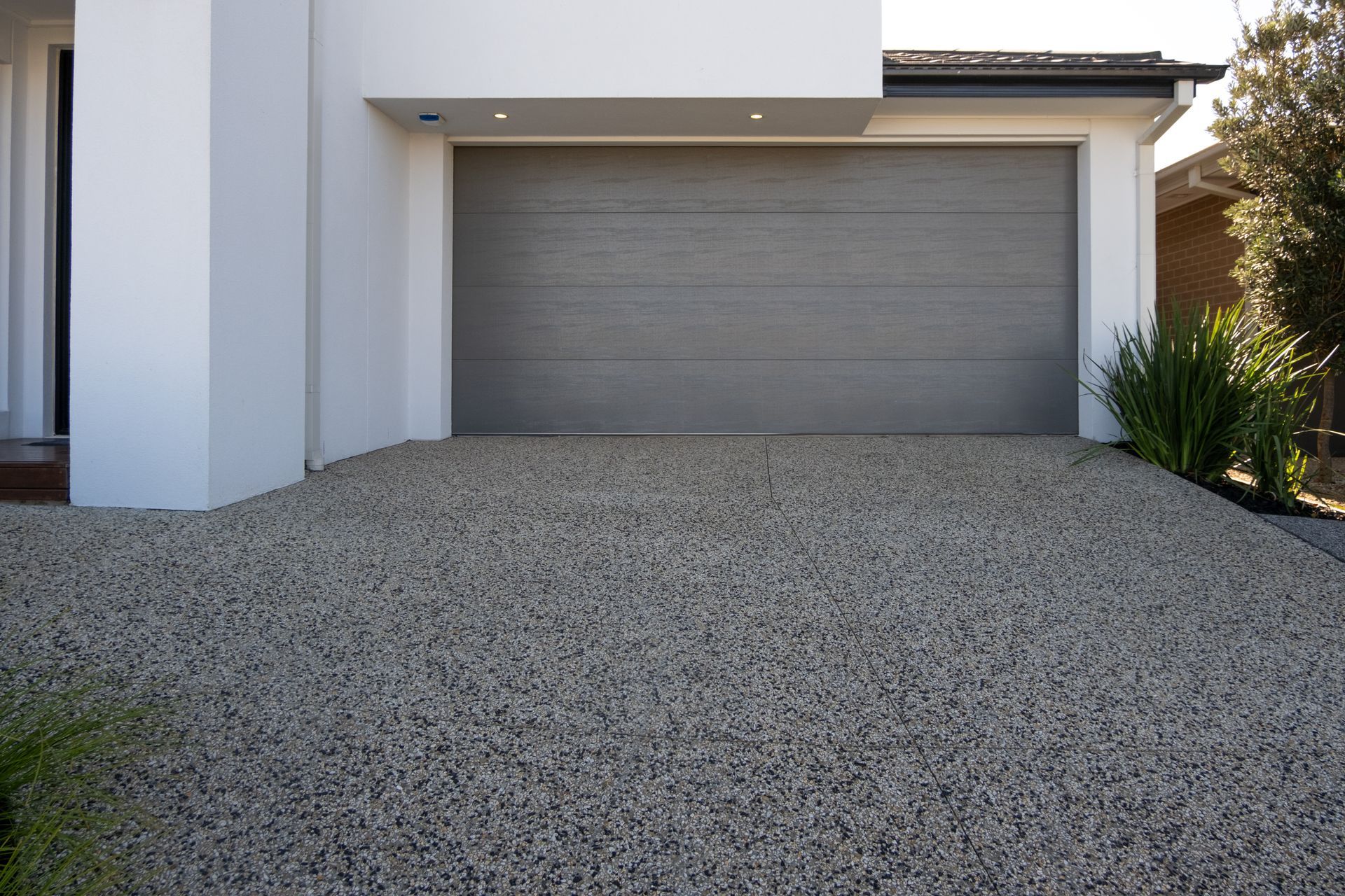 A gravel driveway leads to a gray garage door of a modern white house.
