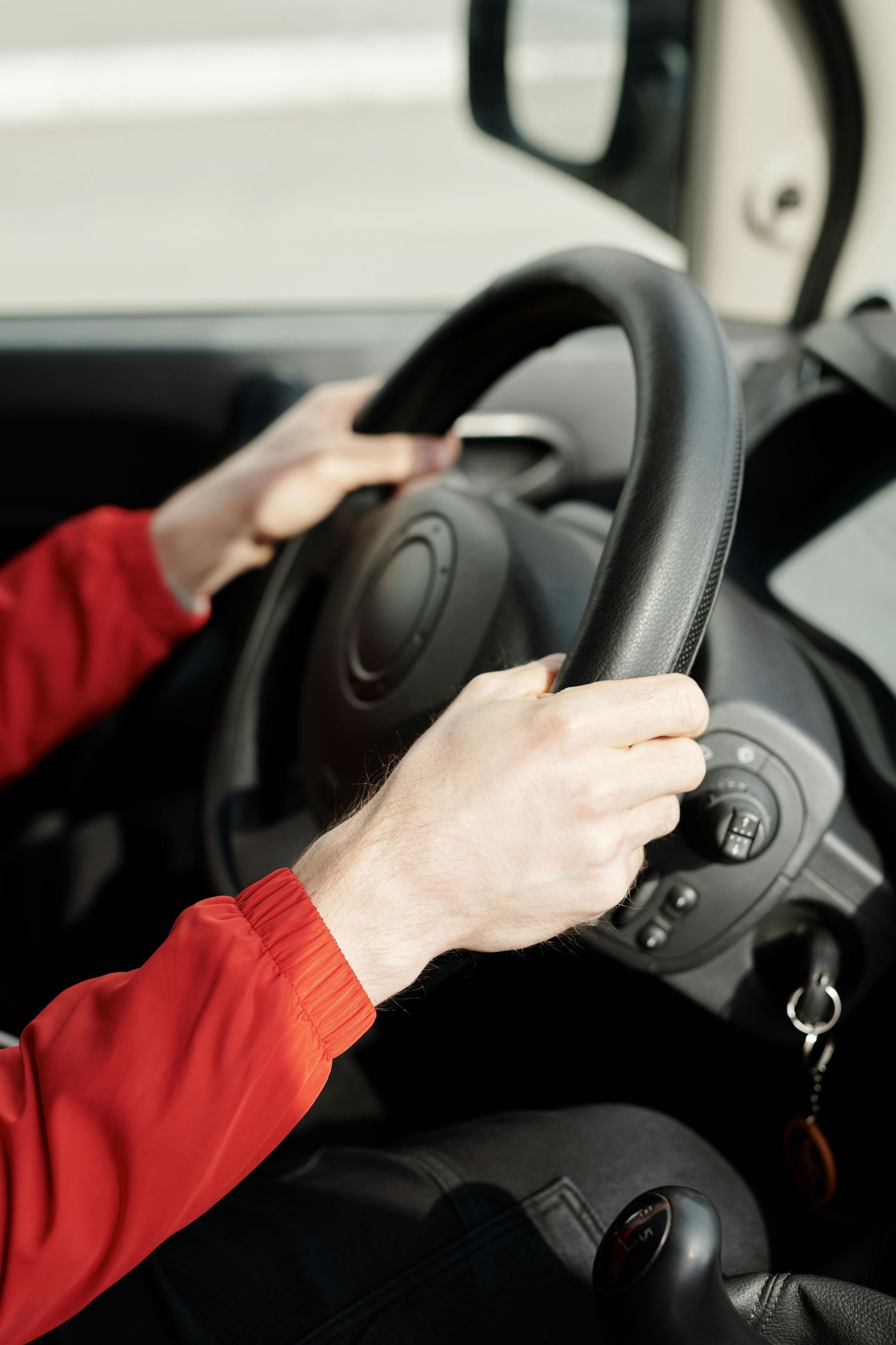 Hands gripping a black steering wheel inside a car, with a red sleeve visible.