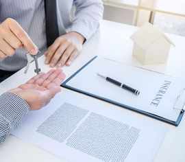 Handing over house keys during a real estate paperwork signing on a desk