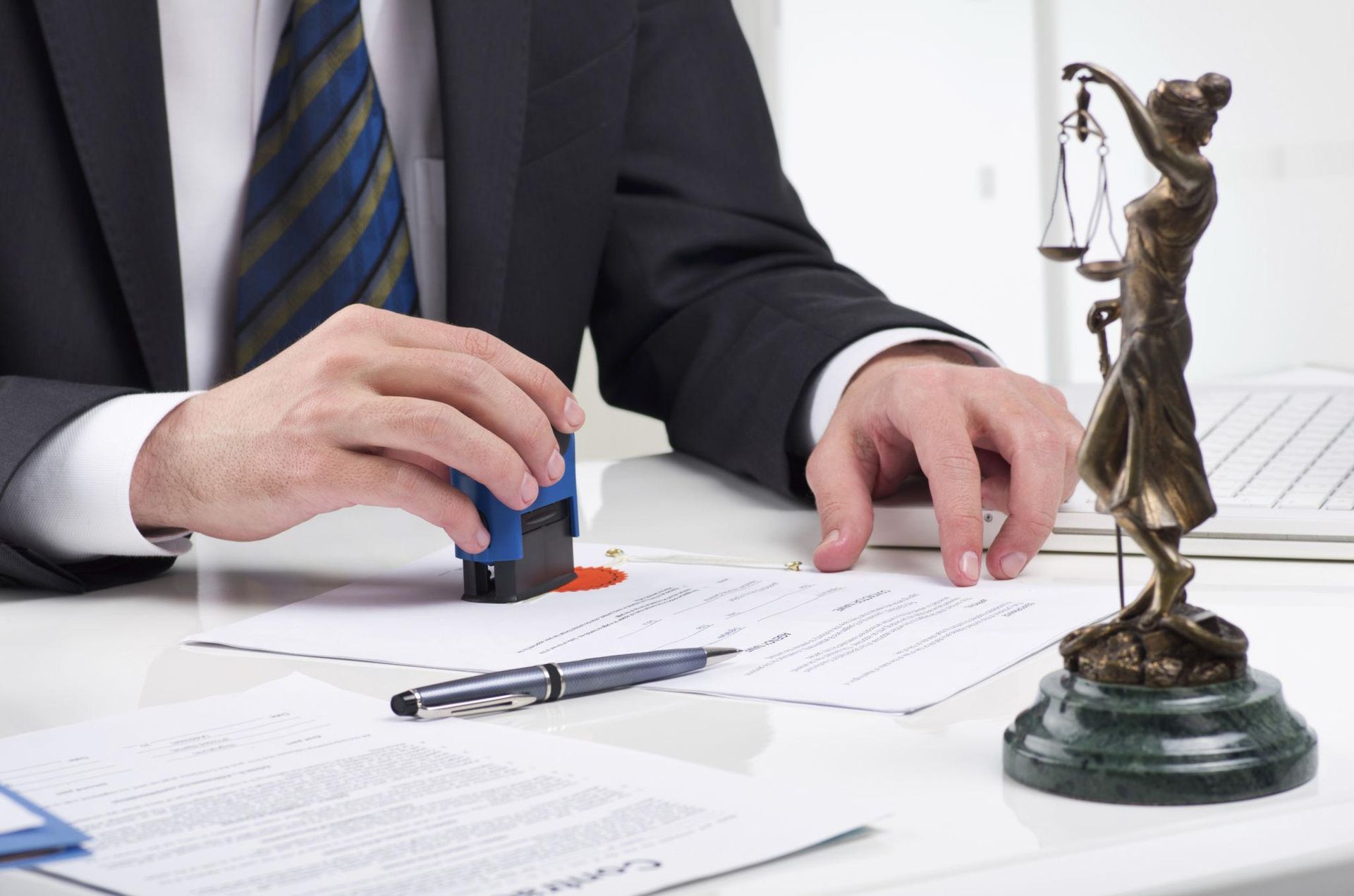 Lawyer stamping a document beside a Lady Justice statue on a desk