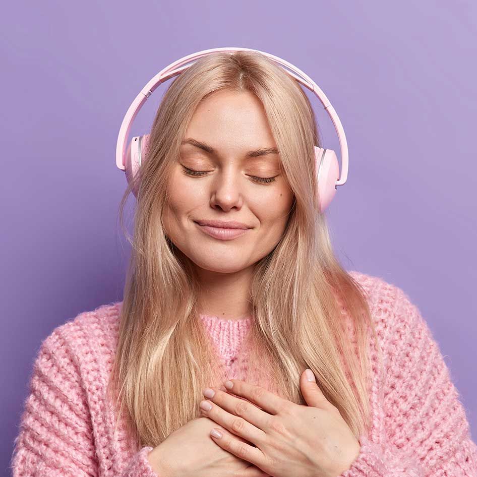 A woman in a pink sweater is wearing pink headphones.