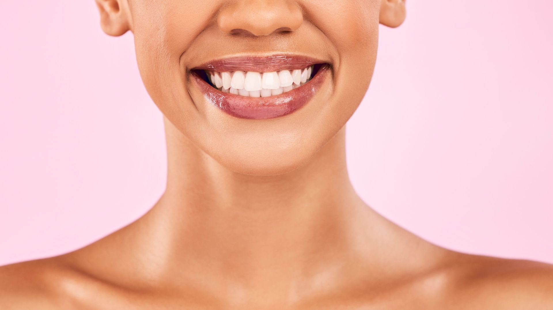 A close up of a woman 's smile with white teeth on a pink background.