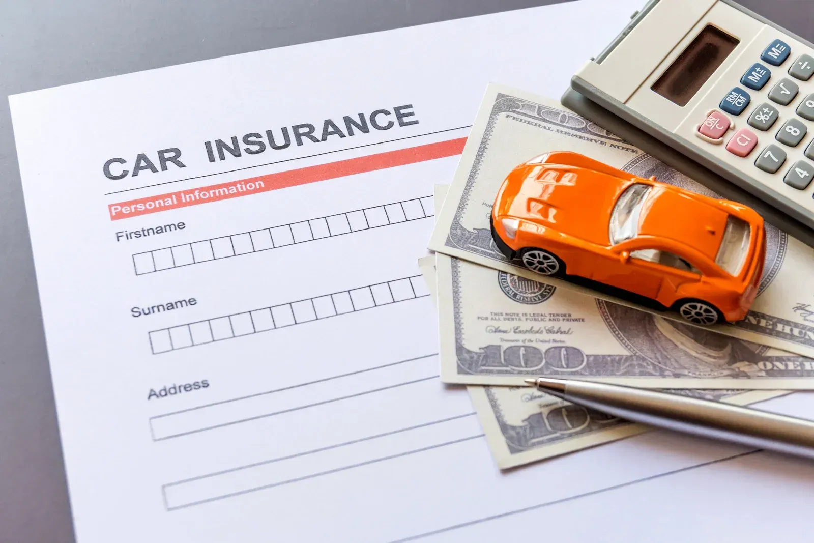 Car insurance form with toy car, money, calculator, and pen.