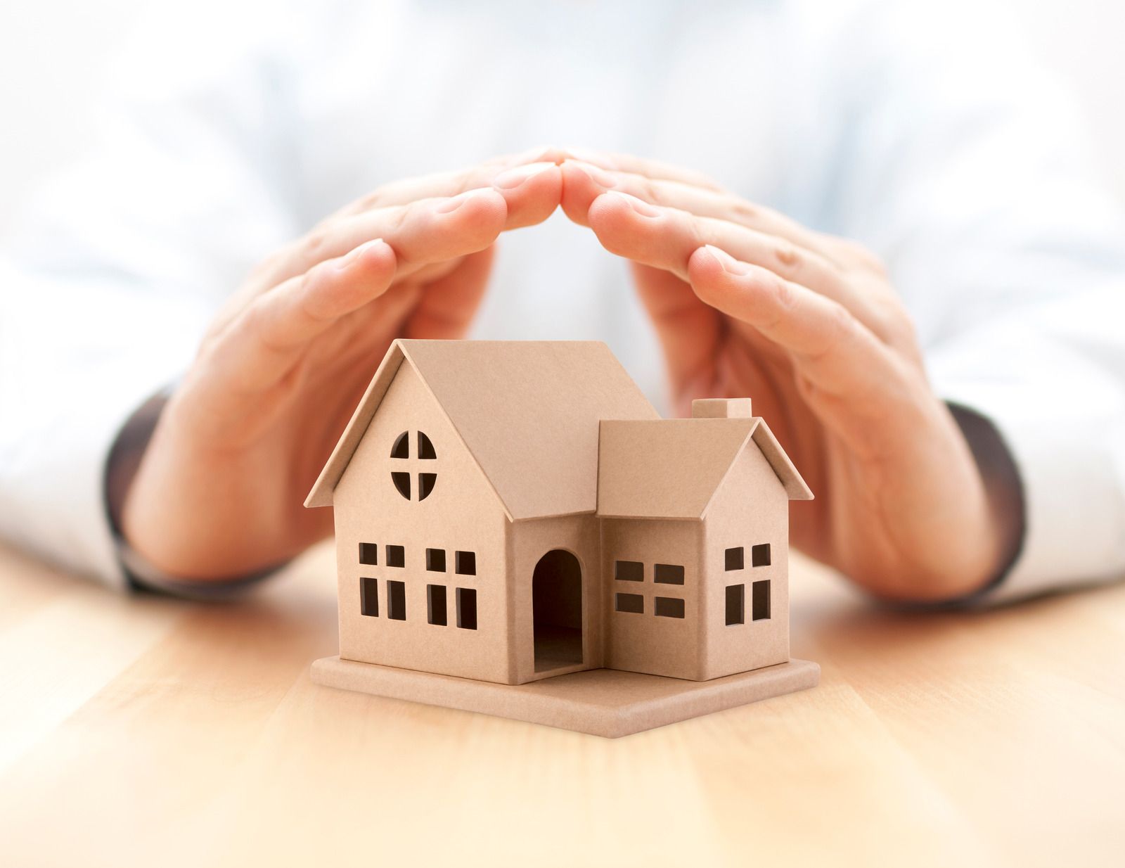 Hands cupping a cardboard house, symbolizing protection and home security.