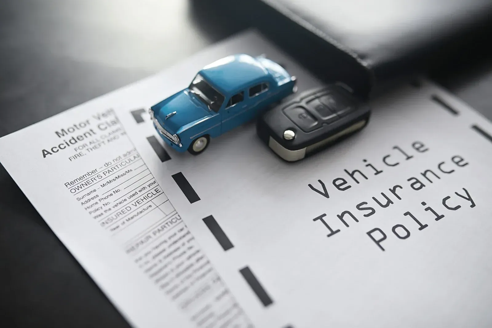 Blue toy car, car keys, and insurance policy on a desk.