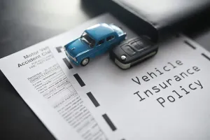 Blue toy car, car keys, and insurance policy on a desk.