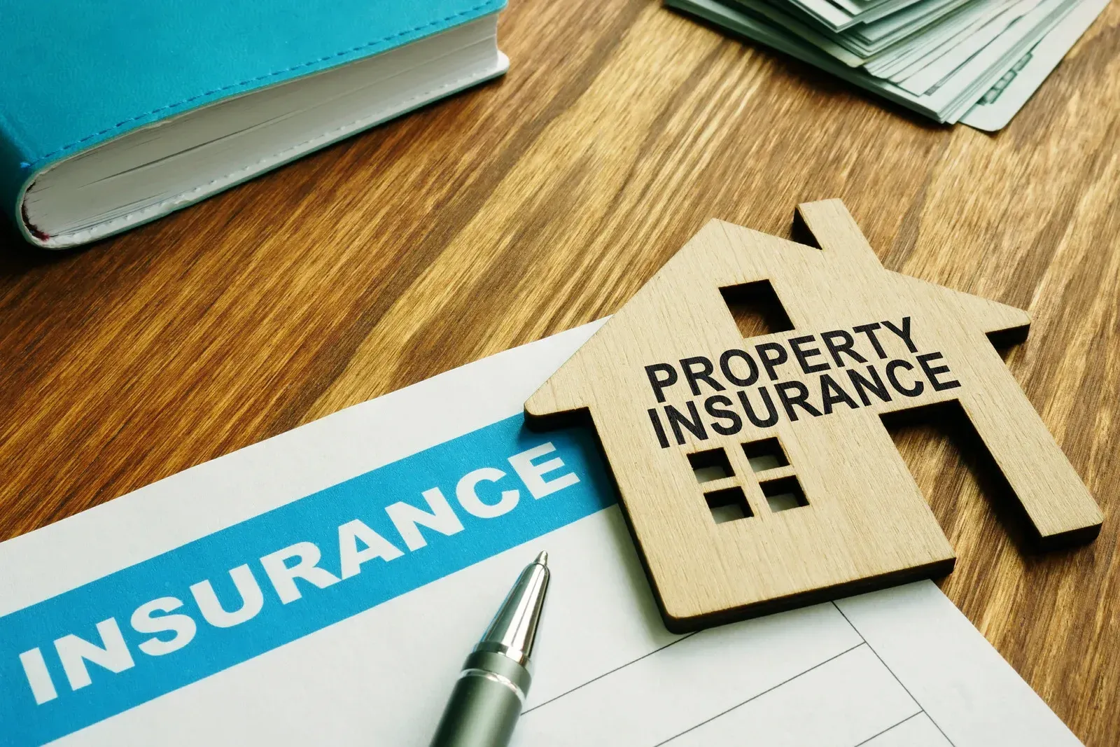 Property insurance document with a wooden house, pen, money, and a book on a wooden table.