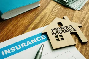 Property insurance document with a wooden house, pen, money, and a book on a wooden table.
