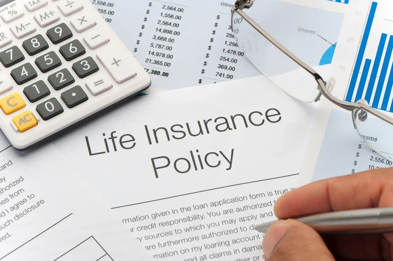 A person reviewing a life insurance policy with a calculator and glasses on a document.