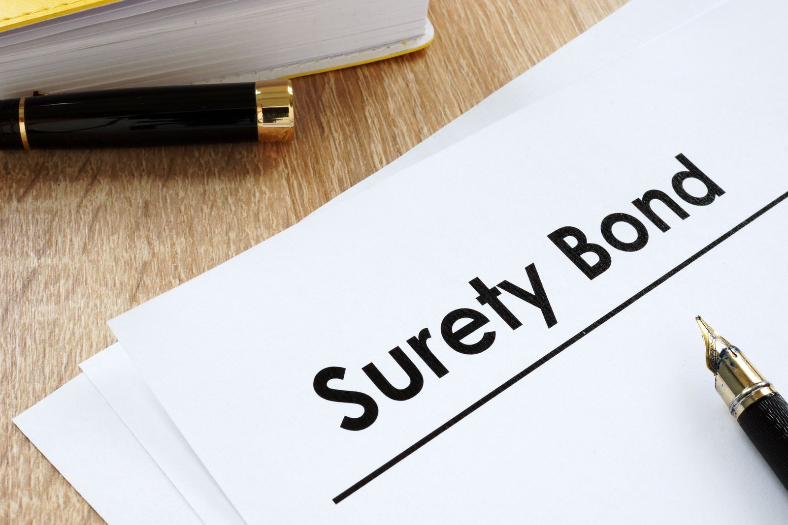 "A document labeled 'Surety Bond' with a pen and other paperwork on a wooden desk."