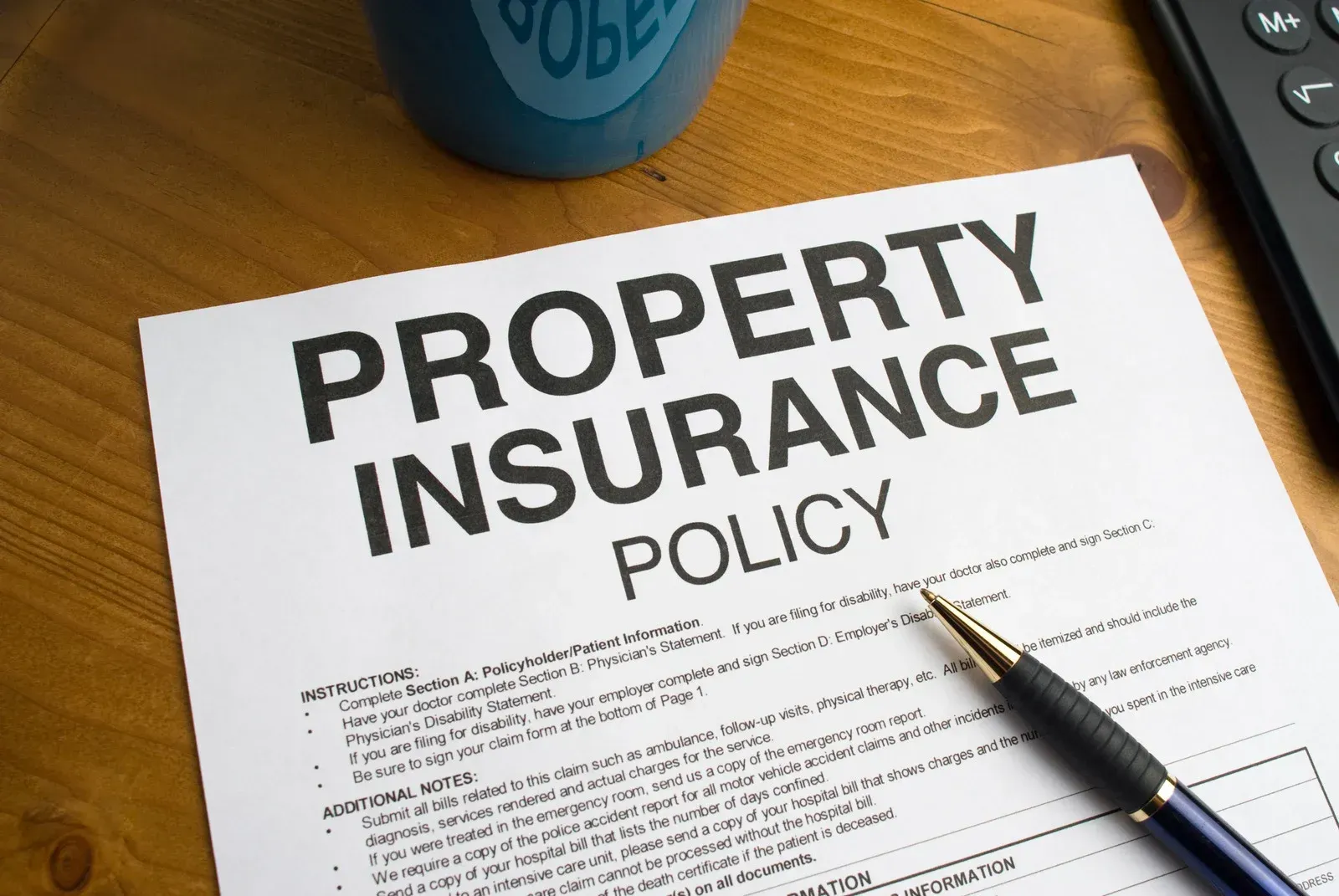 Property insurance policy with pen on wooden desk, blue cup and calculator in the background.