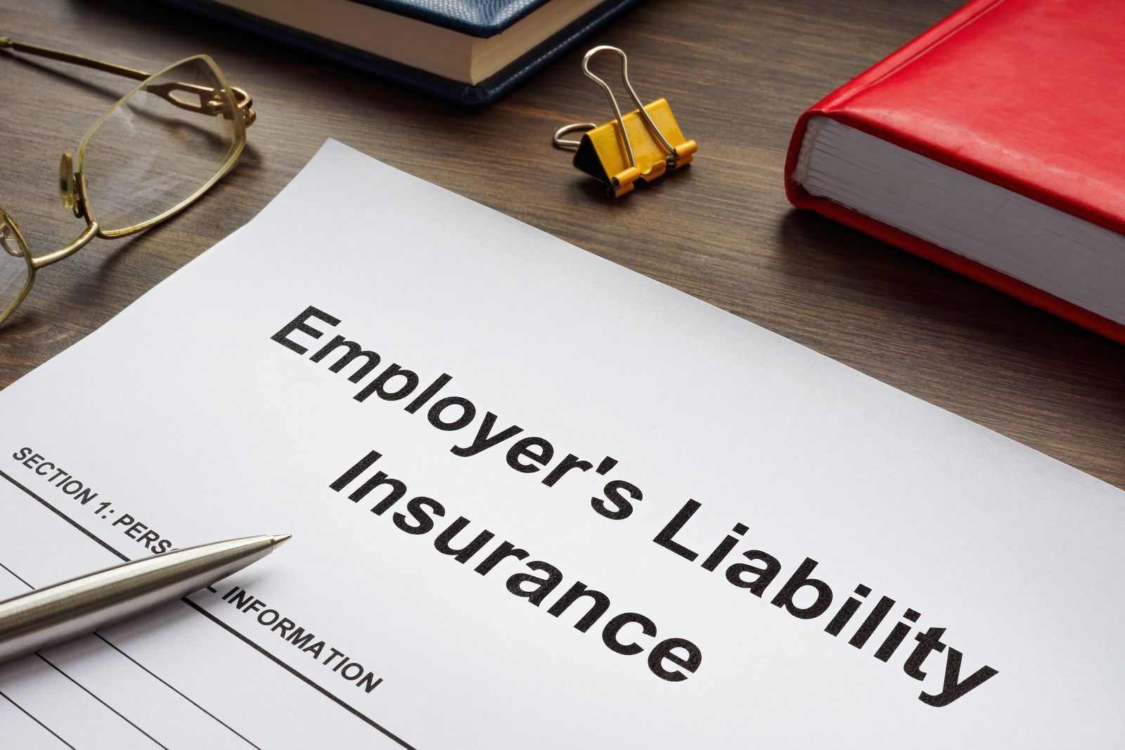 Employer's Liability Insurance document with glasses, pen, binder clip, and books on a wooden desk.