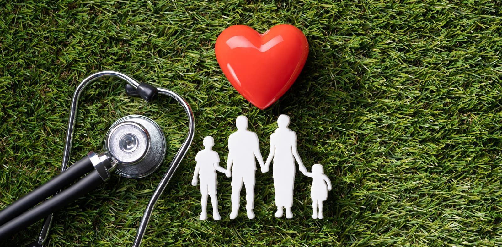 Stethoscope next to a red heart, and family cutout figures on grass.