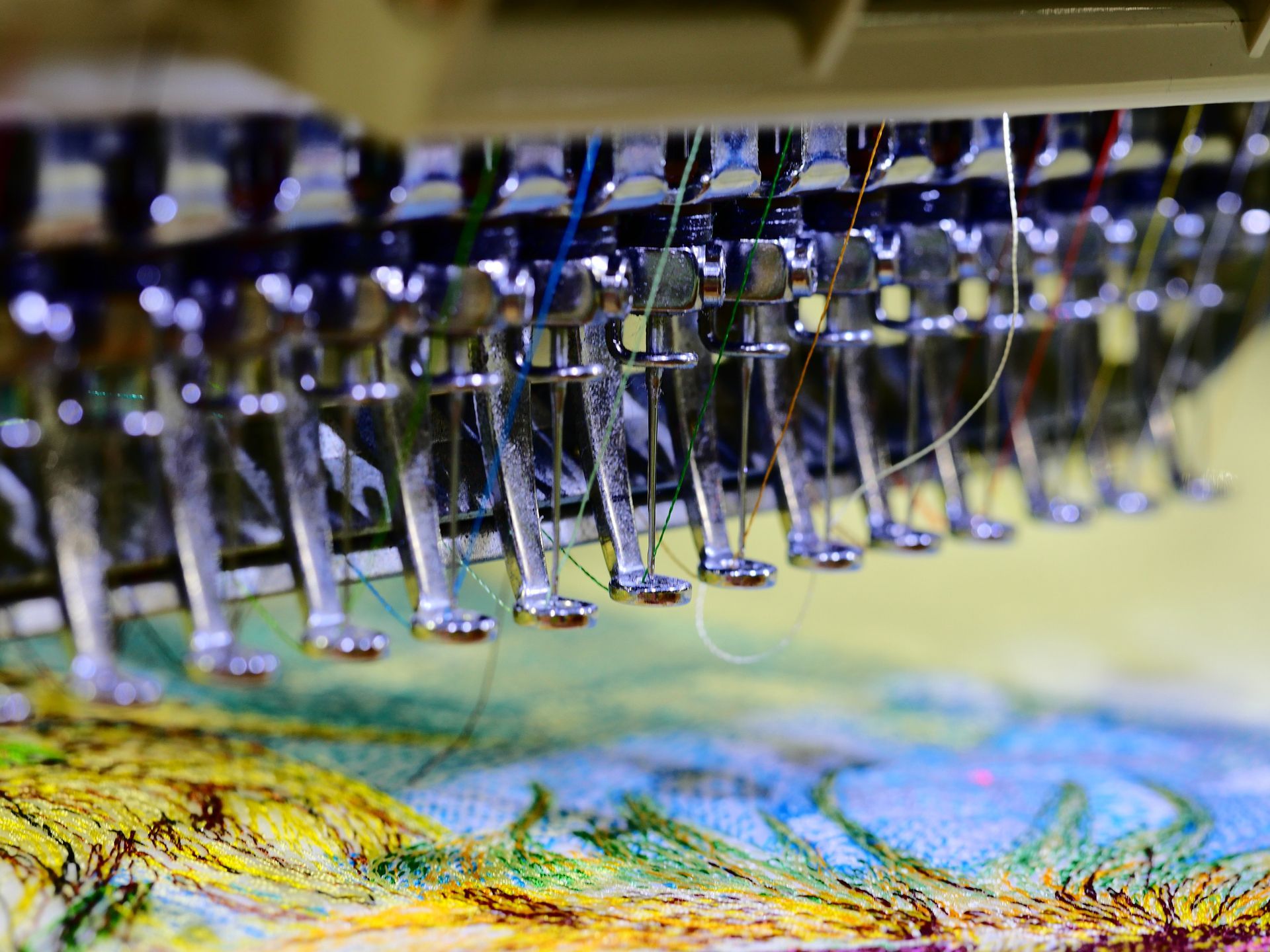 Embroidery machine with multiple needles stitching a colorful floral design. Embroidery machine with multiple needles stitching a colorful floral design.