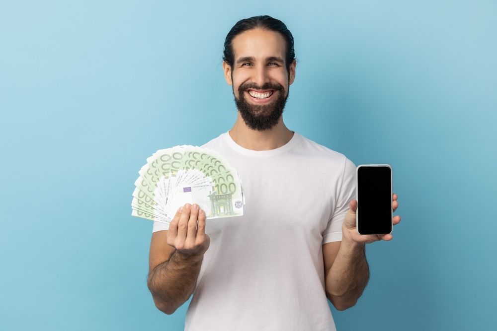 Un uomo tiene in mano un ventaglio di soldi e un telefono cellulare.