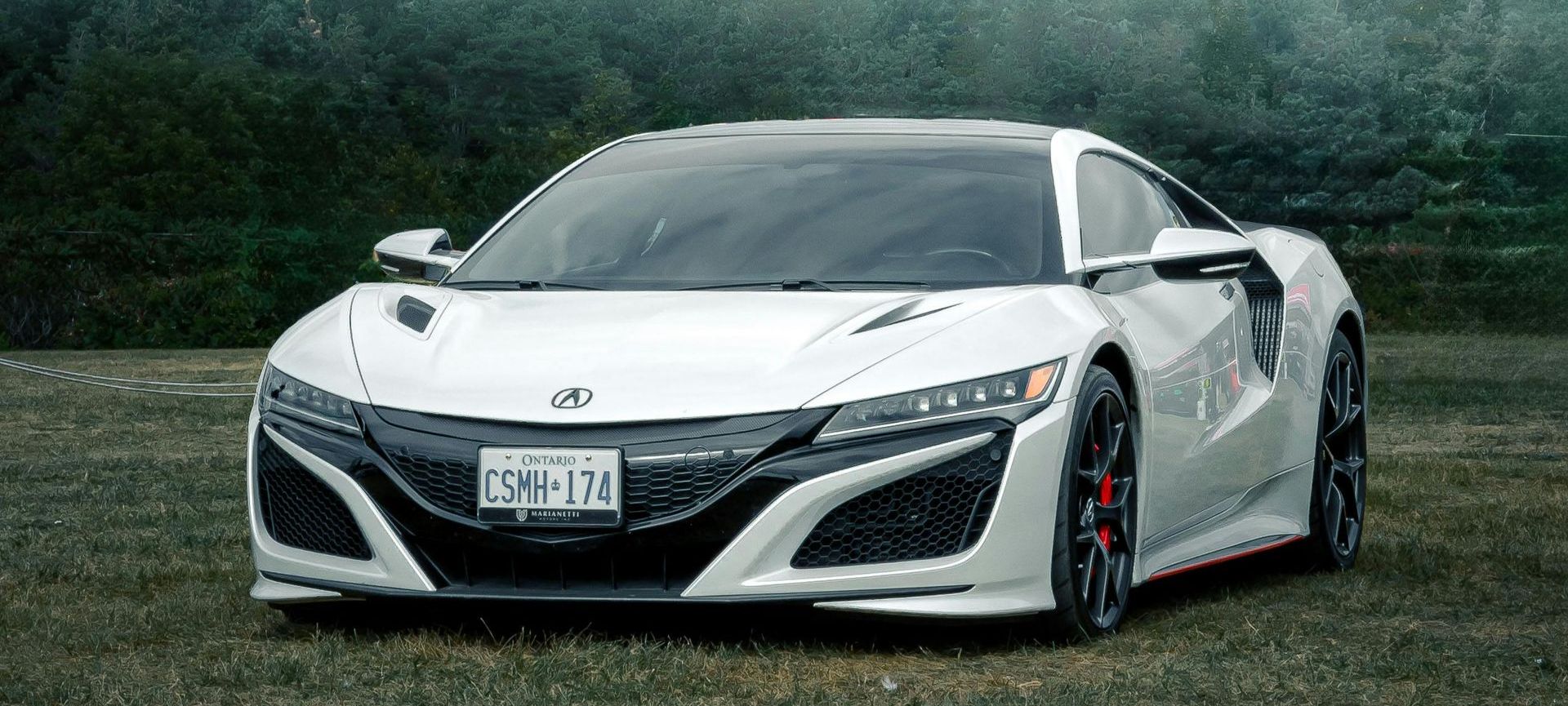 A white sports car is parked in a grassy field.