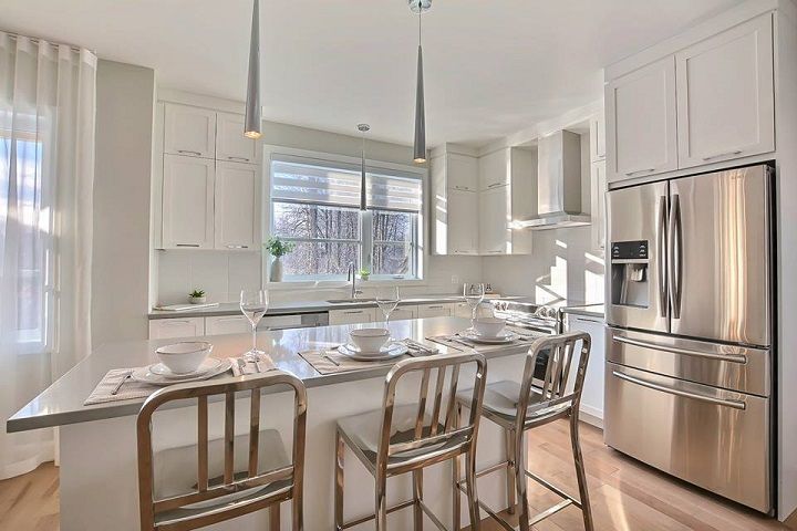 Une cuisine avec armoires blanches, électroménagers en acier inoxydable et un grand îlot.