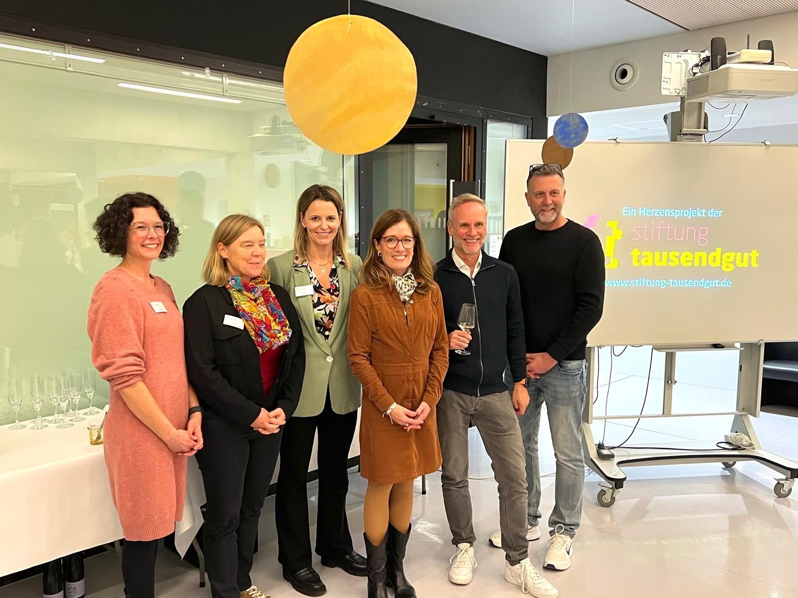 Eine Gruppe lächelnder Menschen steht neben einem Schild mit einem gelben Ballon.