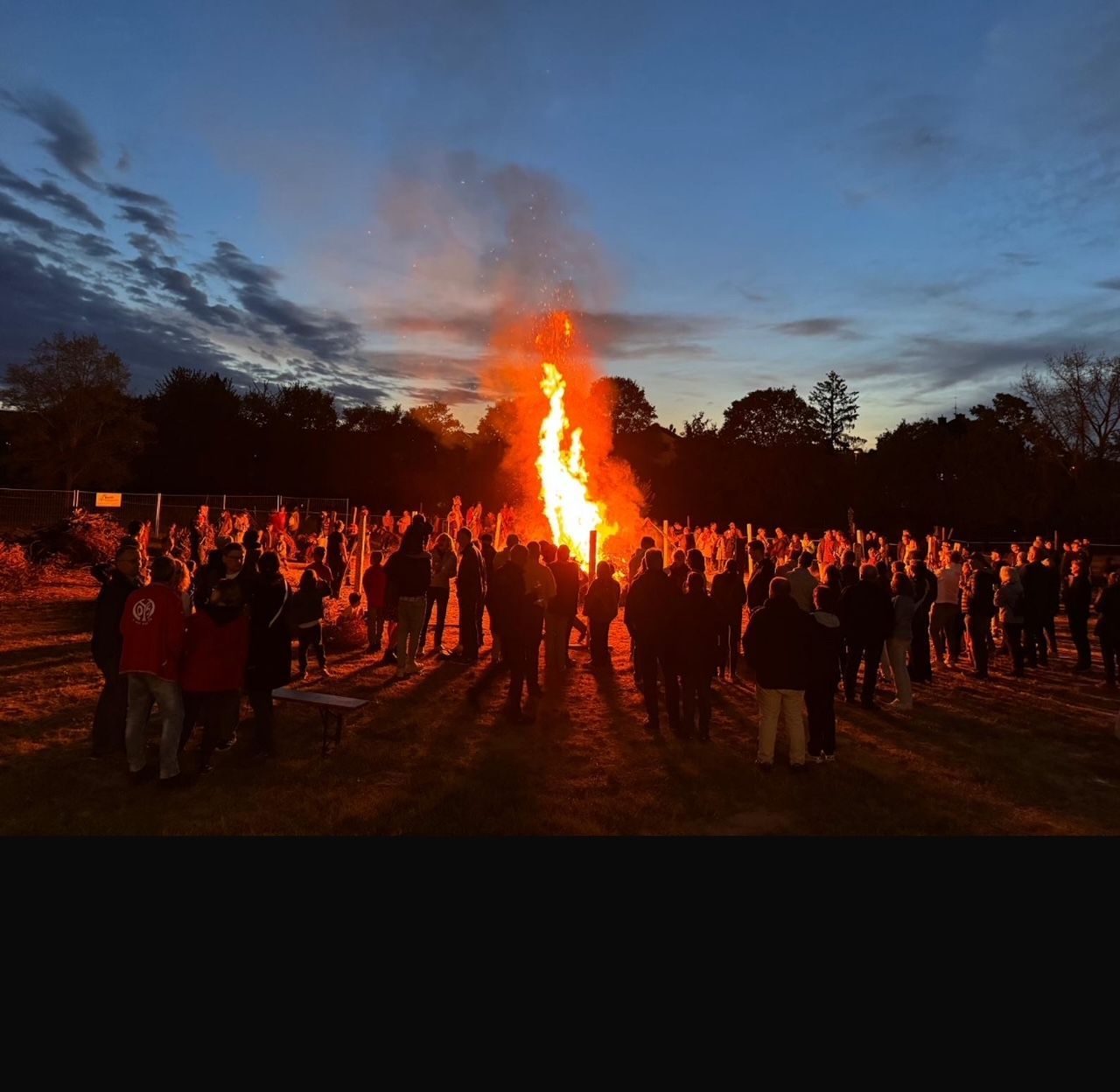 Eine Gruppe von Menschen steht nachts um ein großes Feuer herum.
