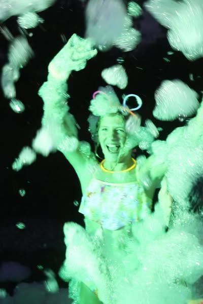 A woman is joyfully dancing in glowing green foam.