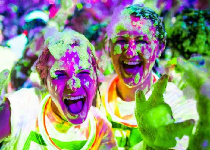 Two people are covered in glow in the dark foam and laughing.