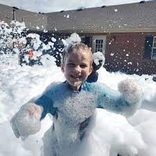 A young boy is standing in a pile of foam in front of a house.
