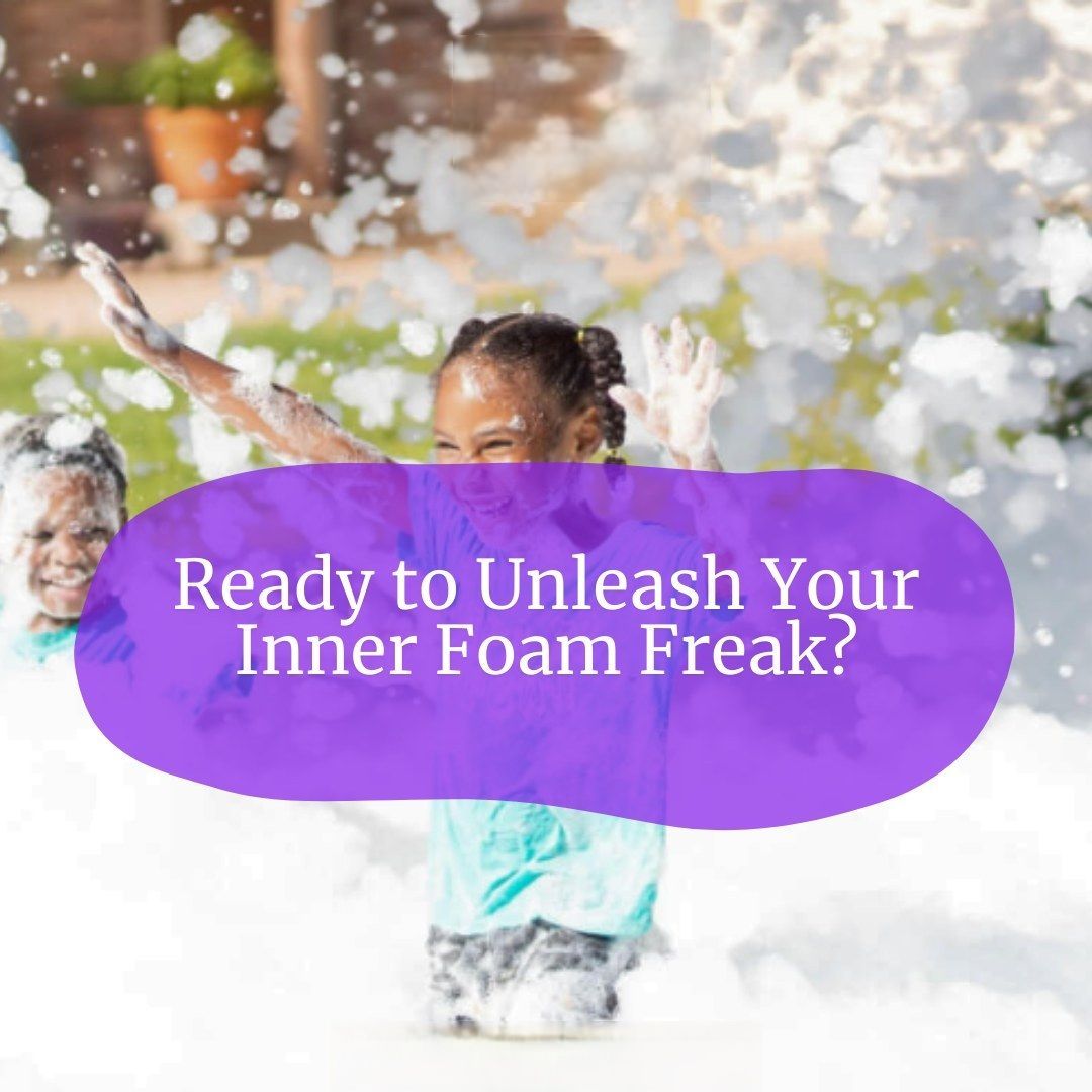 A girl is playing in foam with a purple sign that says ready to unleash your inner foam freak ?