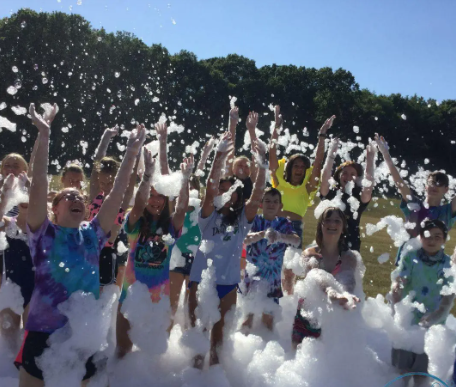 A group of children are standing in a field covered in foam.