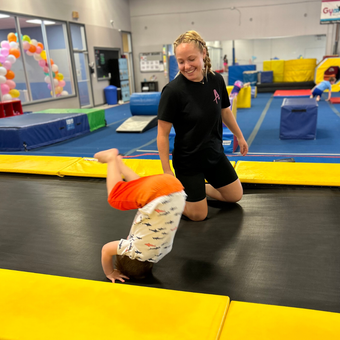 A woman is helping a child do a handstand on a trampoline.