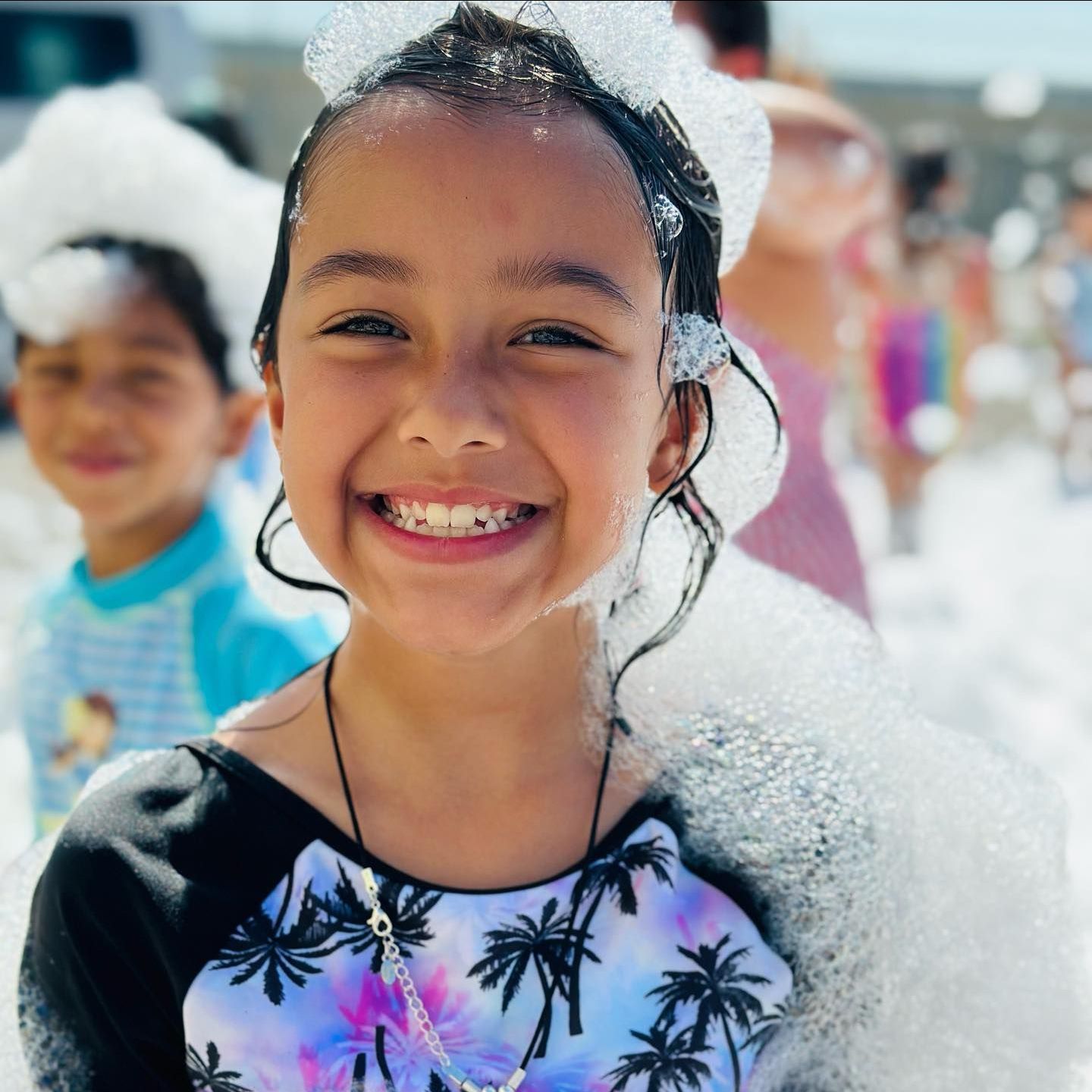 A little girl is sitting at a table with her hands covered in foam.