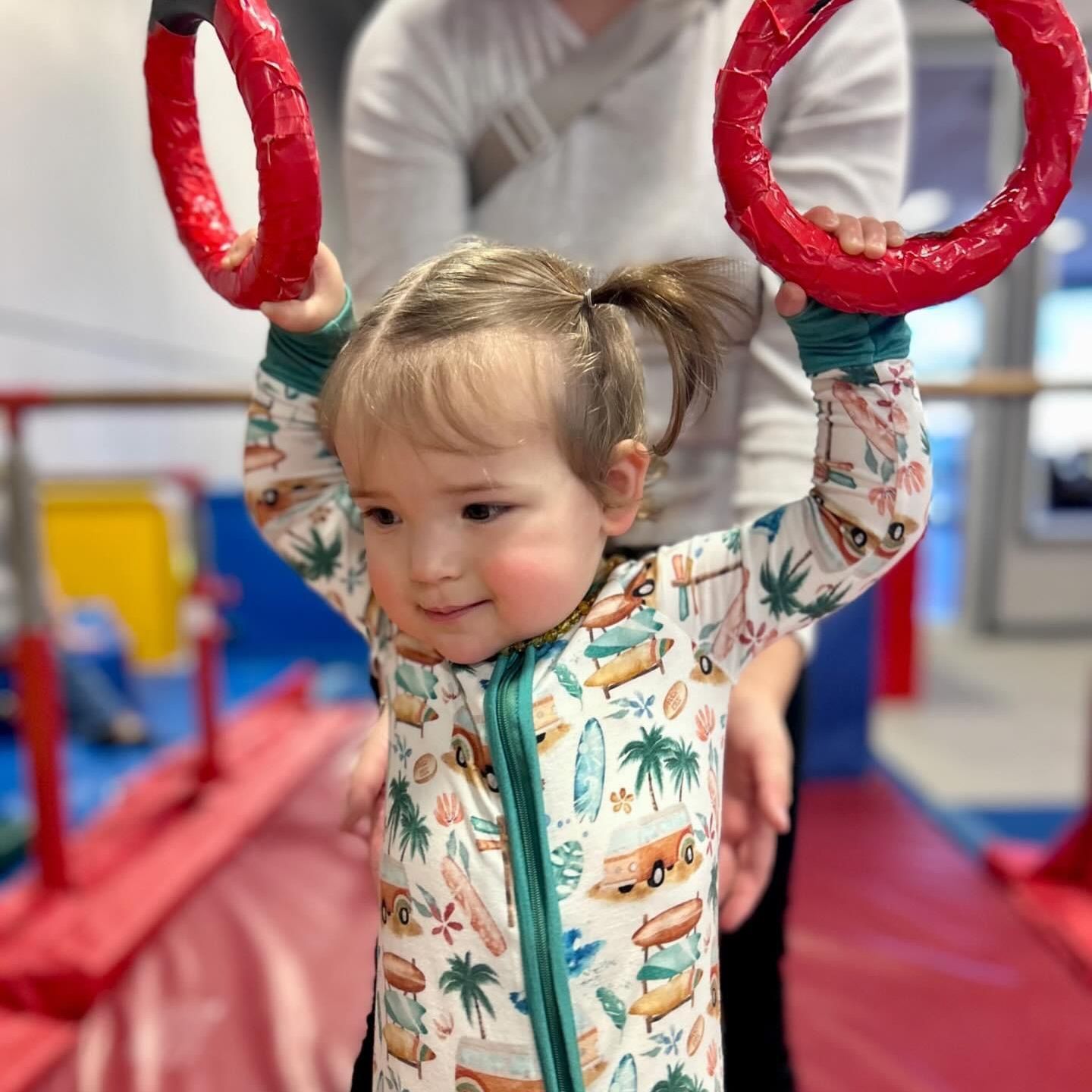 A little girl is holding two red gymnastic rings over her head