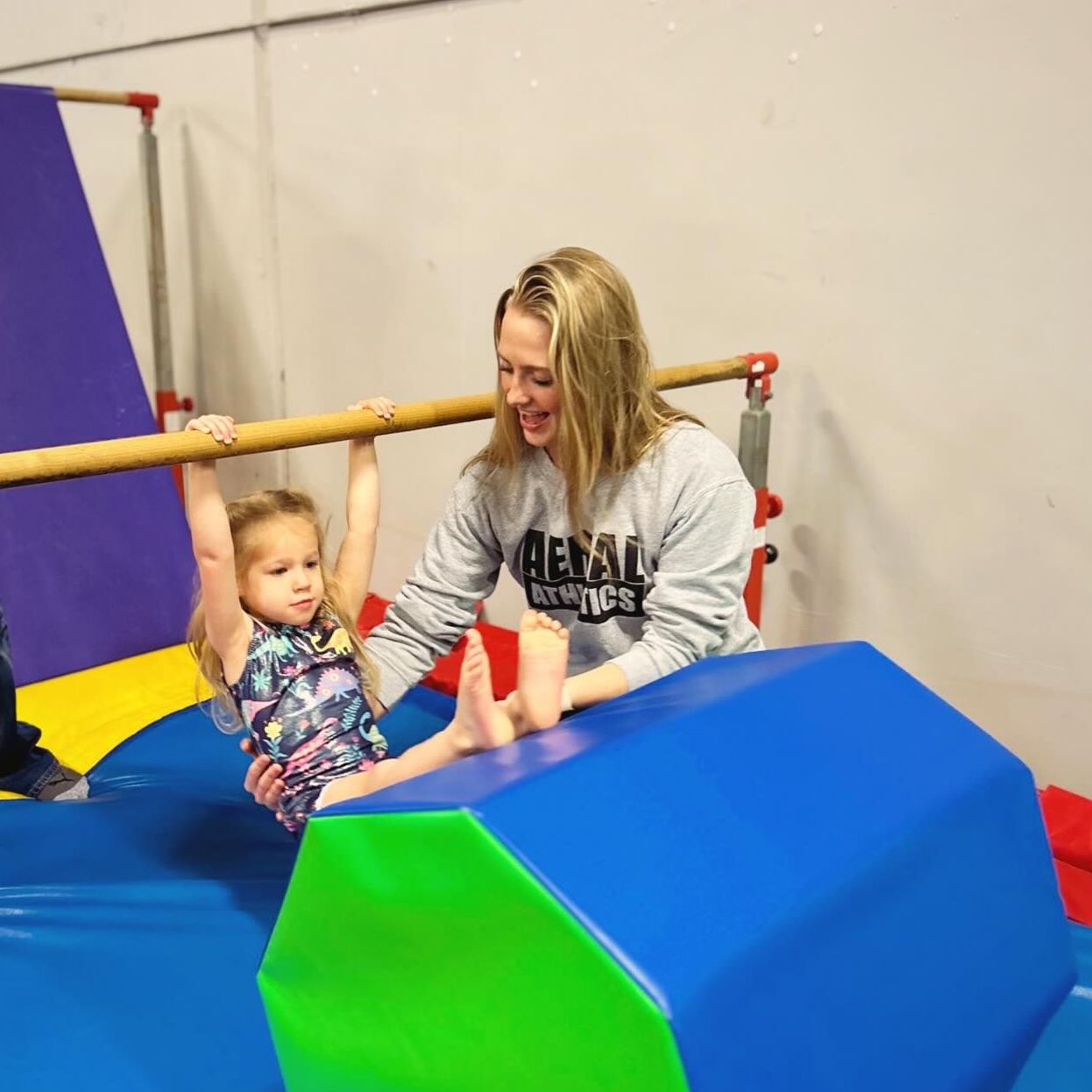 A woman is playing with a little girl on a blue mat.