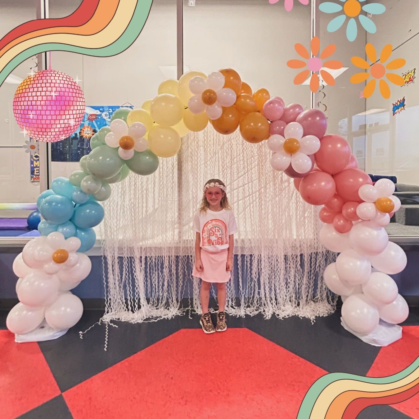A little girl is standing in front of a balloon arch