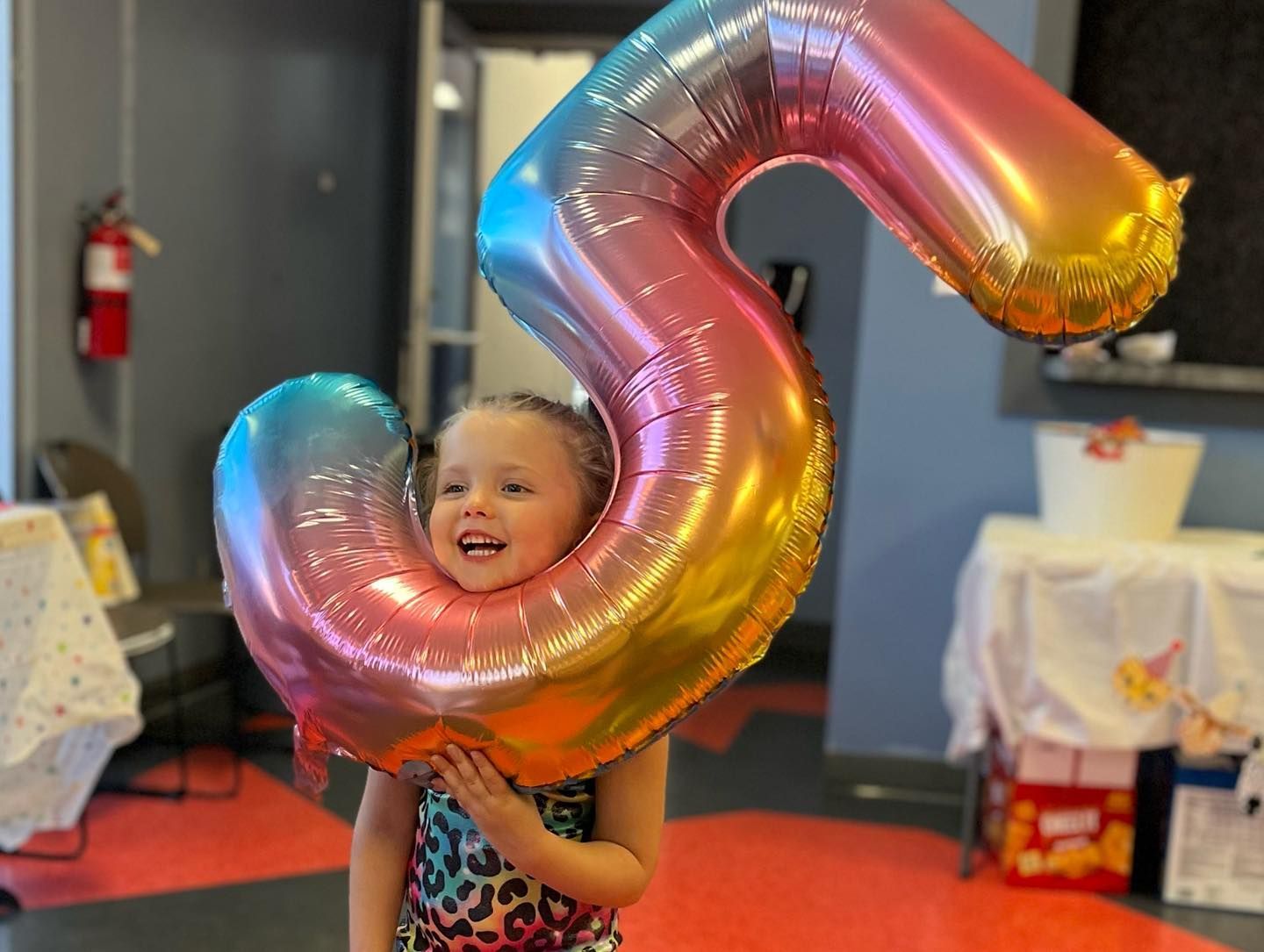 A little girl is holding a large balloon in the shape of the number five.