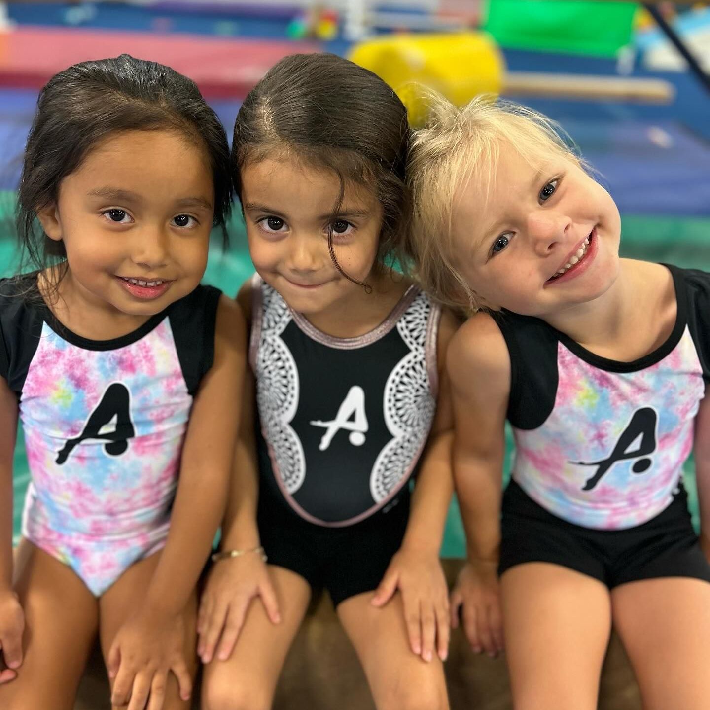 Three little girls wearing leotards with the letter a on them