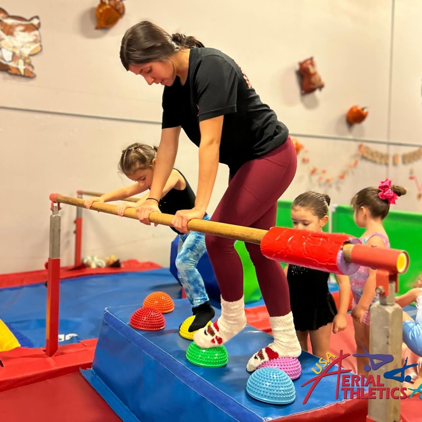 A woman is standing on a bar in a gym with children