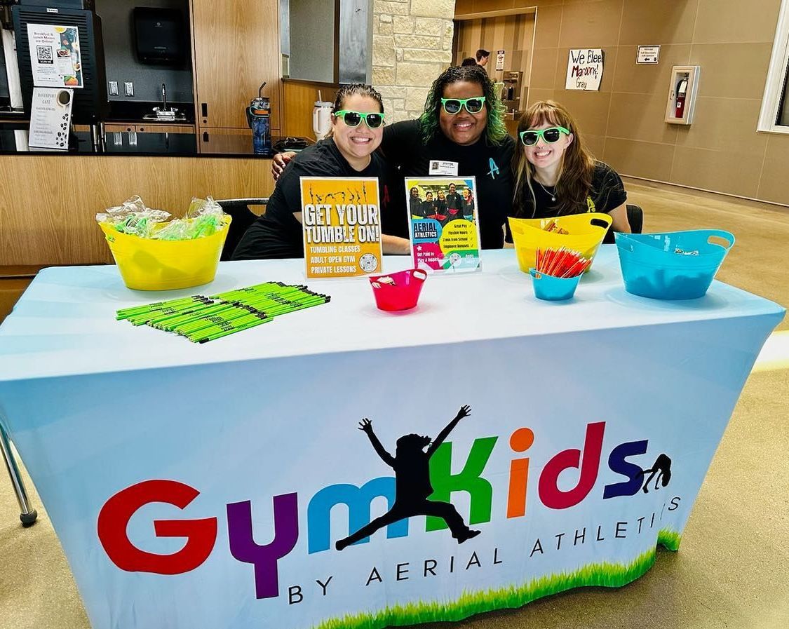 A group of people standing around a table that says gymkids on it.
