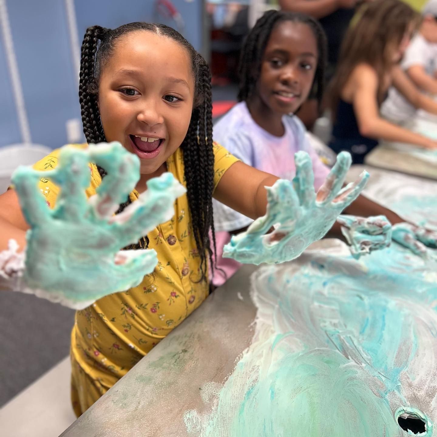 A little girl is sitting at a table with her hands covered in foam.