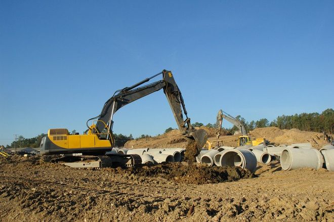 Excavator digging trenches for large concrete pipes