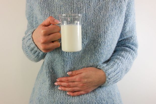 Una donna con un maglione blu tiene in mano un bicchiere di latte.