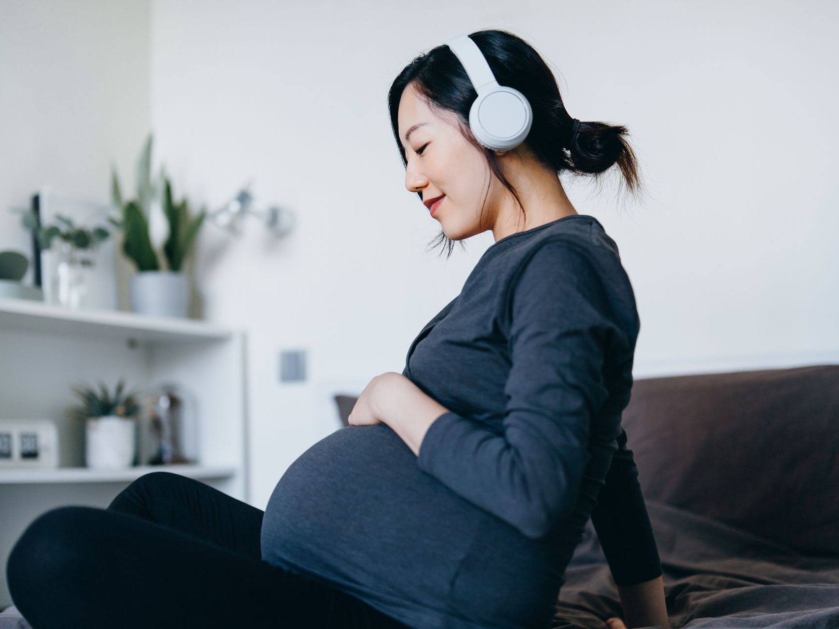 Una donna incinta seduta su un divano con le cuffie.