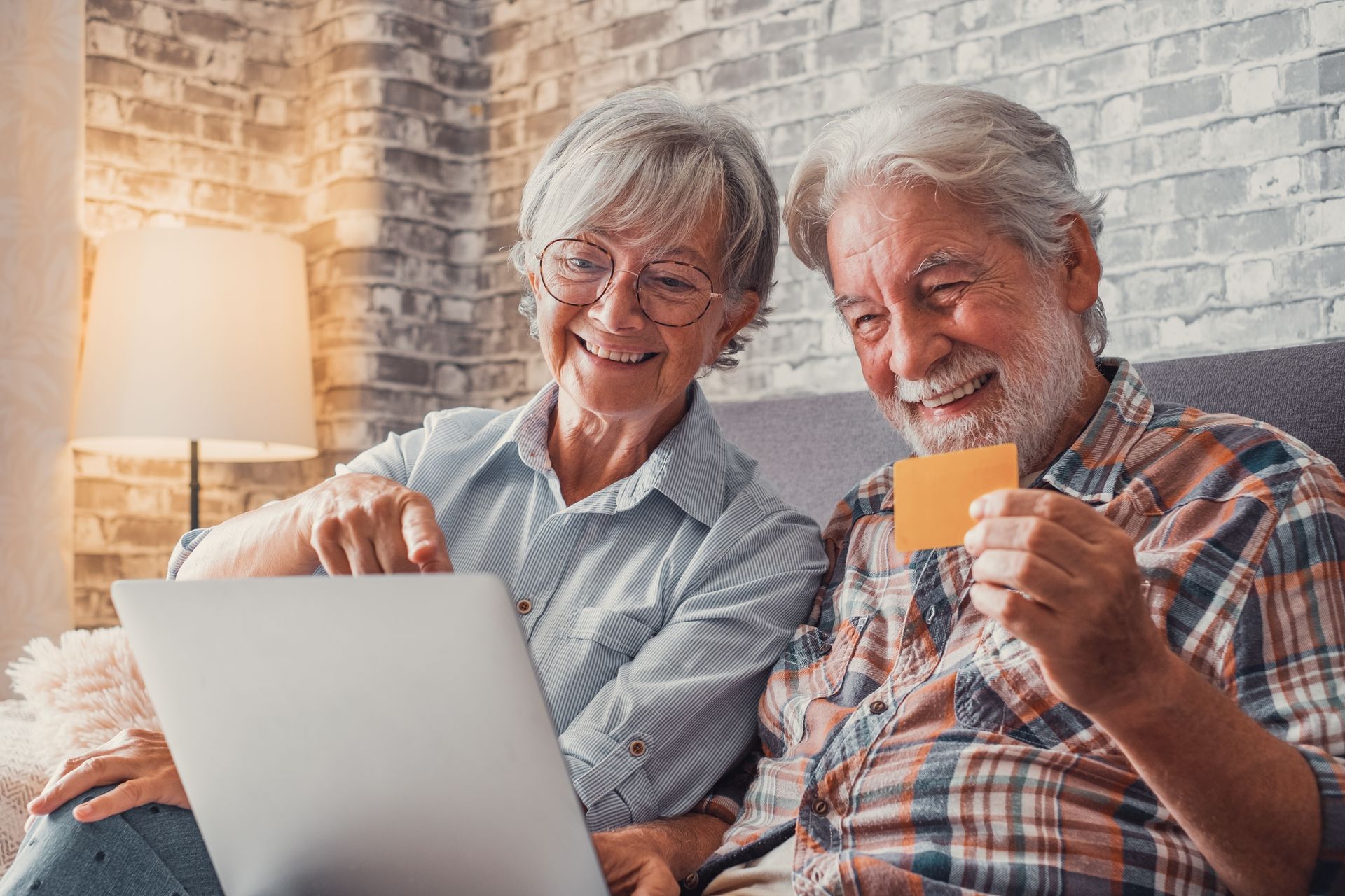 A man and a woman are sitting on a couch looking at a laptop computer.
