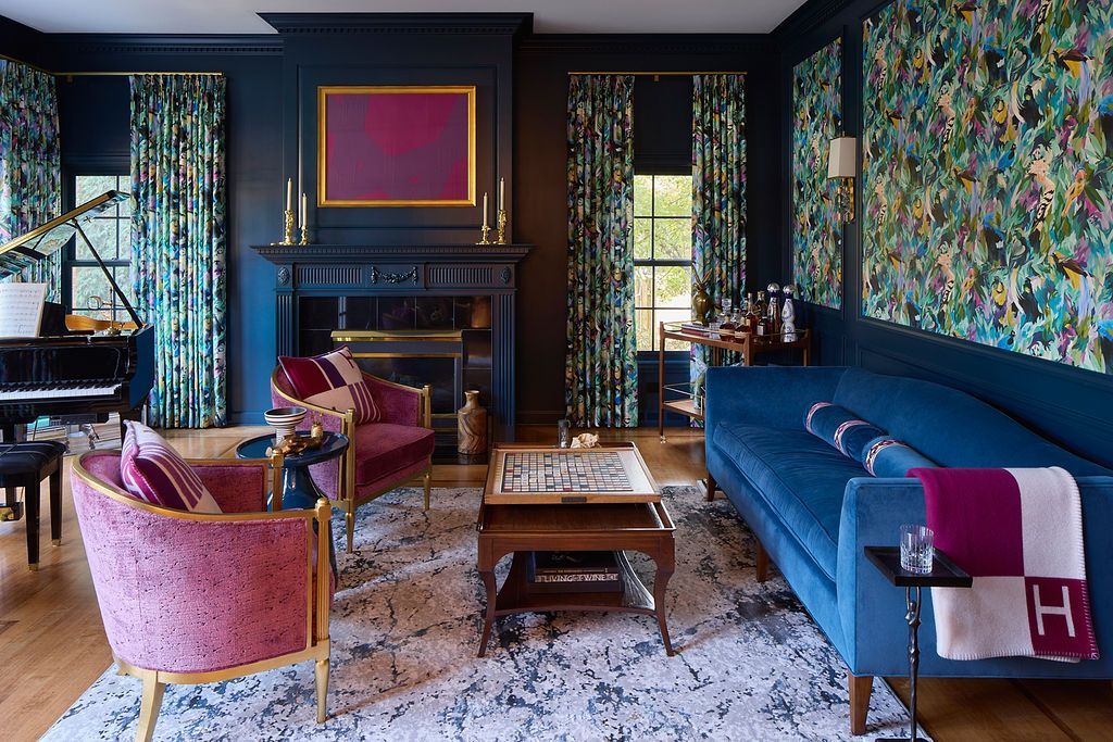 Living room with blue walls, floral curtains, pink chairs, a blue sofa, and a fireplace.